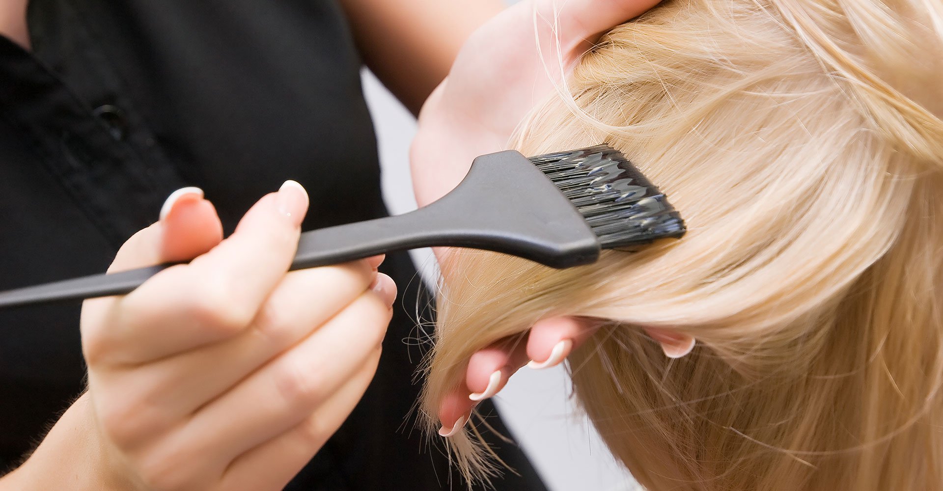 Profissional passando produto em cabelo loiro